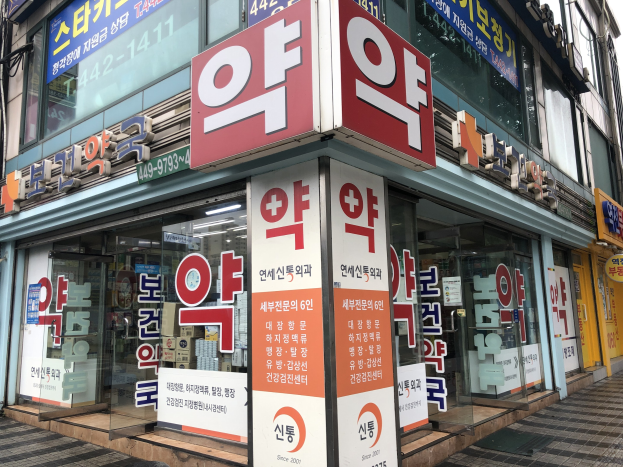 Außenansicht einer modernen Glaswand-Apotheke in Seoul, Südkorea, mit Texttafeln, die "Südkoreas erste Apotheke in Seoul, Südkorea" lesen.