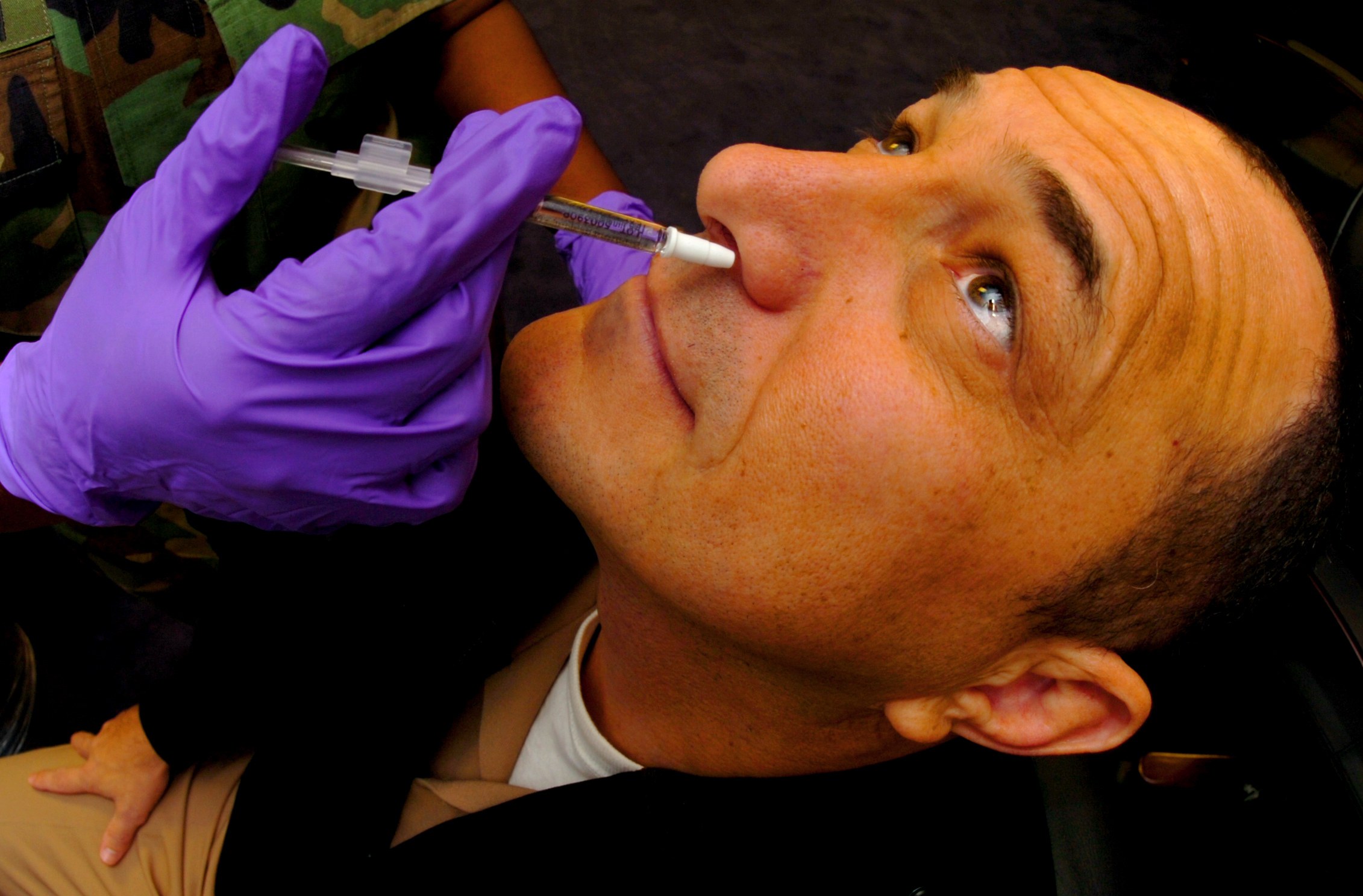 Ein Arzt in lila Handschuhen verimpft einem Mann ein Vakzin durch eine Injektion in den Mund.
