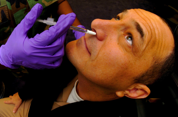 Ein Arzt in lila Handschuhen verimpft einem Mann ein Vakzin durch eine Injektion in den Mund.