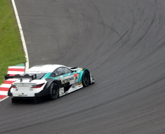 Ein silberner Mercedes-AMG GT3 Rennwagen auf einer Rennstrecke mit Text auf der Karosserie und Gras links daneben.