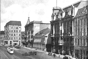 Ein Schwarz-Weiß-Foto einer Straßenkreuzung in Stuttgart, Deutschland, circa 1900, mit Fahrzeugen, Gebäuden mit Fenstern, Laternenpfählen und einem bewölkten Himmel.