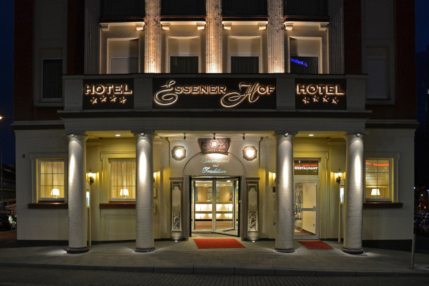 Das Essenerhof Hotel in Berlin, Deutschland, ein mehrstöckiges Gebäude mit Fenstern, Türen, Säulen, Lampen und einem Namensschild, das sichtbar ist, und eine Straße mit Fahrzeugen auf der rechten Seite, unter einem klaren Himmel.