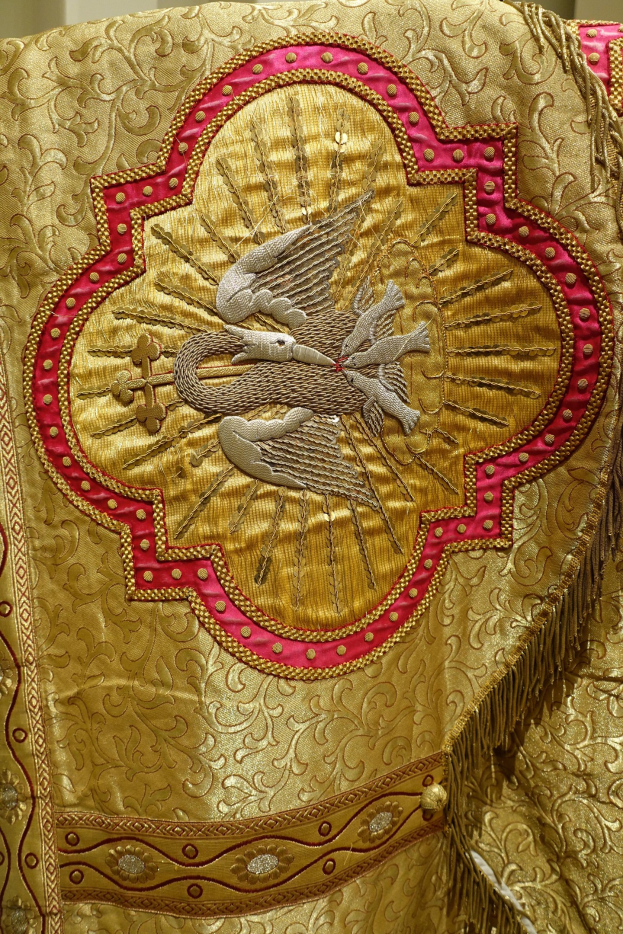 Nahaufnahme eines Priestergewandes mit goldenen und roten Stickereien an einer Wand im Hintergrund