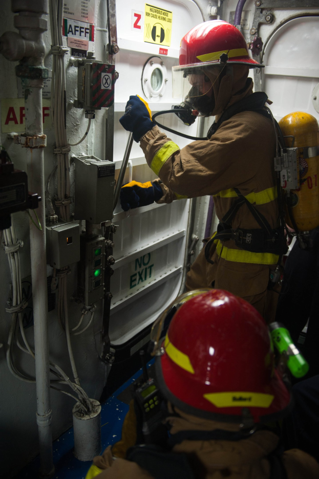 Zwei Feuerwehrleute in Schutzausrüstung arbeiten an Gerät zwischen Rohren und Maschinen.