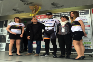 Eine Gruppe von Menschen auf einem Podium stehend, mit einem Mann in der Mitte, der einen Blumenstrauß hält, und einem Schild dahinter mit der Aufschrift "Giro d'Italia 2016."