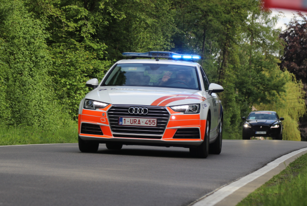 Polizeiauto (Audi A4) mit zwei Insassen auf einer grasbewachsenen Straße neben einem Wald unter einem klaren blauen Himmel.