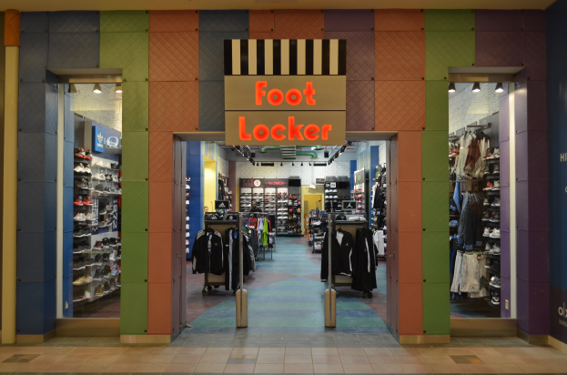 Innenansicht eines Foot Locker-Schuhgeschäfts mit Kleidung an Bügeln und Regalen unter Ladeneinrichtung.