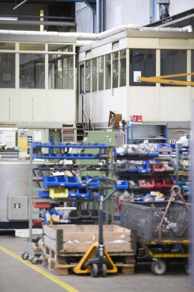 Großes Lagerinnere mit verschiedenen Geräten einschließlich fahrbaren Wagen, Schränken und einer Box, mit einer verglasten Wand und freiliegenden Rohren im Hintergrund.