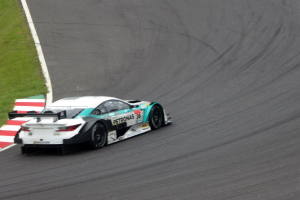 Ein Mercedes-AMG GT3 Rennauto fährt auf einer Rennstrecke mit Text auf dem Auto und Gras links.