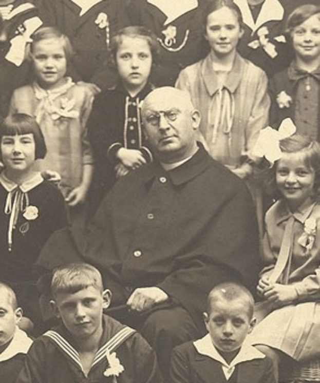 Ein Schwarz-Wei├č-Foto eines ernst aussehenden Mannes, der in der Mitte sitzt und von einer Gruppe Kinder umgeben ist, die ihn bewundernd anschauen.