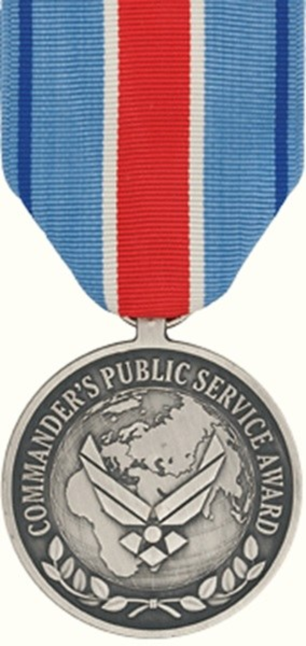 Eine silberne Medaille mit einem rot-weiß-blauen Band, auf dem "Commander's Public Service Award" steht, vor einem weißen Hintergrund.