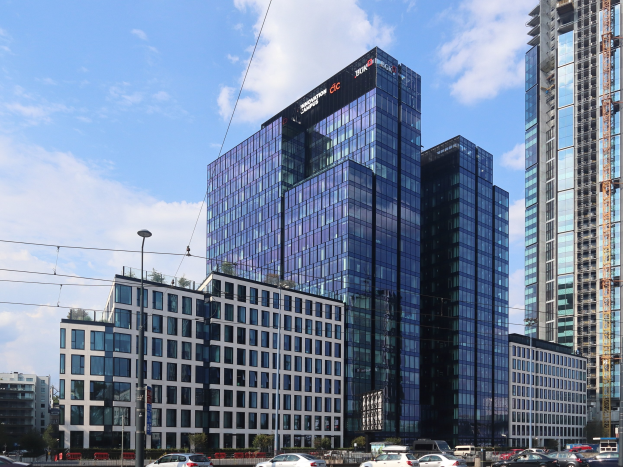 Zentrale der Deutschen Bank in Frankfurt, Deutschland, ein großes mehrfenstriges Gebäude umgeben von städtischer Infrastruktur und Grünflächen unter einem bewölkten Himmel.