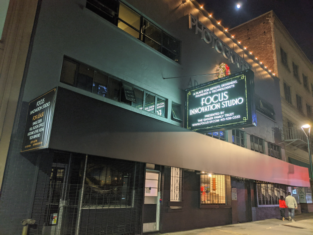 Nachtansicht des Focus Innovation Studios in New York City mit beleuchteten Gebäuden, sichtbaren Fenstern, Namensschildern, Passanten auf dem Gehweg und Straßenlaternen.