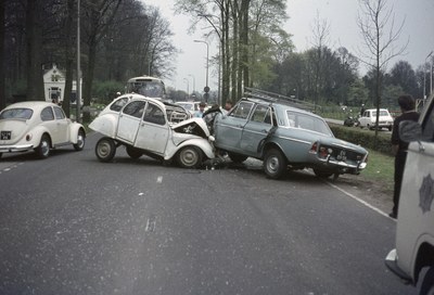 Zwei beschädigte Autos am Straßenrand mit Menschen in der Nähe, vor einem Hintergrund aus Bäumen, Polen, Gebäuden und einem klaren blauen Himmel.