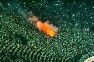 Luftaufnahme einer großen Menge von Menschen in einem Stadion mit einem zentralen Feuer, das die Umgebung erhellt.
