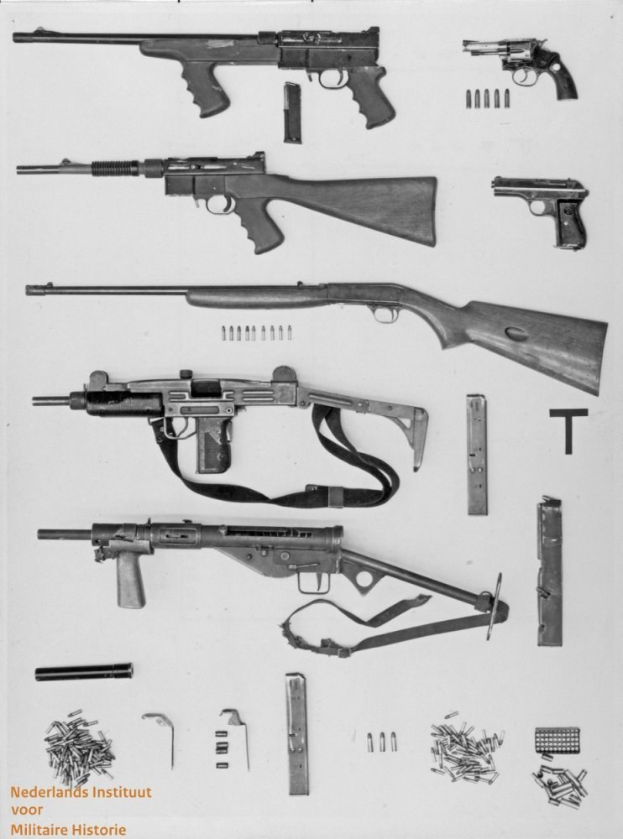 Schwarz-weiß-Foto von verschiedenen Feuerwaffen, einschließlich einer Maschinengewehr, mit verstreuter Munition und Gegenständen und Text unten.
