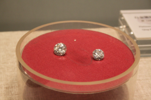 Ein Paar Diamant-Ohrringe in einer durchsichtigen Glasbox auf einem Tisch, funkelnd und das Licht reflektierend.