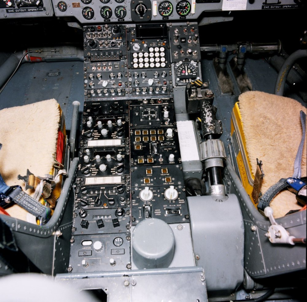 Ein Cockpit eines Flugzeugs mit einer Instrumententafel voller Knöpfe, Schalter und Tasten sowie einem Sitz für Passagiere.