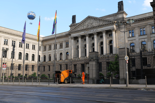 Großes modernes Gebäude mit vielen Fenstern, als Bundestag in Berlin identifiziert, umgeben von Straßeninfrastruktur und Passanten unter einem bewölkten Himmel.