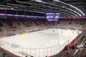 Eishockeyspiel in einer großen Arena zwischen den St. Louis Blues und Detroit Red Wings, mit Zuschauern auf Sitzen und Stehplätzen in der Nähe der Eisfläche umgeben von einem Zaun und einem Display.