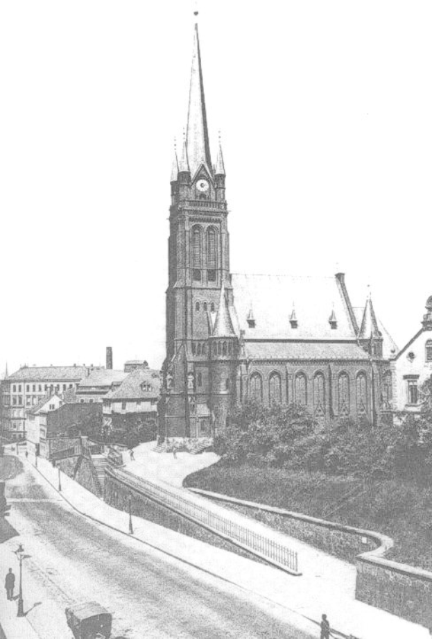 Schwarz-weiß-Foto einer Stadtstraße mit St. Peter Kirche im Hintergrund, gesäumt von Gebäuden, Bäumen, Fahrzeugen und Passanten.