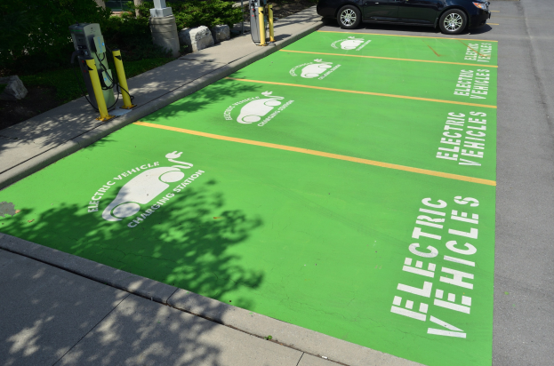 Elektroauto an einer Ladestation mit grünem Bodenmattenmarkierer auf einem Parkplatz mit Bäumen und umgebenden Objekten.
