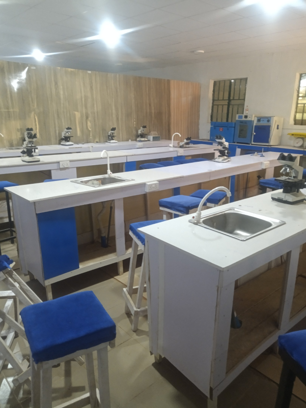 Ein Labor mit blauen Hockern, weißen Arbeitsplatten, einem Spülbecken mit Wasserhähnen, Maschinen, Fenstern an einer Wand und Deckenleuchten, Teil der Universität für Wissenschaft und Technologie in Ahmedabad.