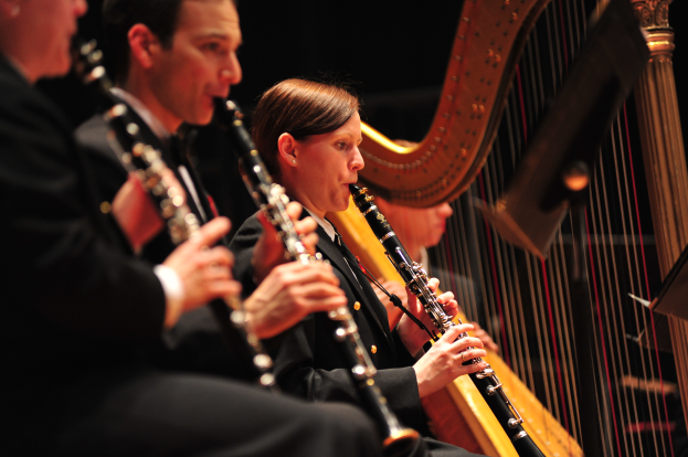 Eine Gruppe von Menschen auf einer Bühne Klarinetten spielend, mit einem Musikständer im Vordergrund und einem dunklen Hintergrund.