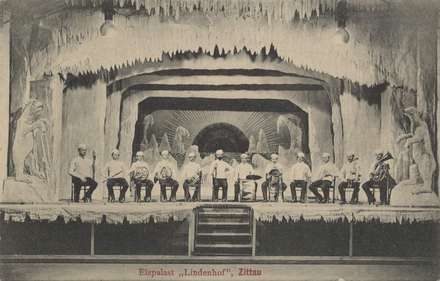 Altes Schwarz-Weiß-Foto einer Gruppe von Menschen auf einer Bühne mit Musikinstrumenten, Treppen führen hinauf und Skulpturen auf beiden Seiten, mit Text "Lindenhof, Zittau, Deutschland" unten.
