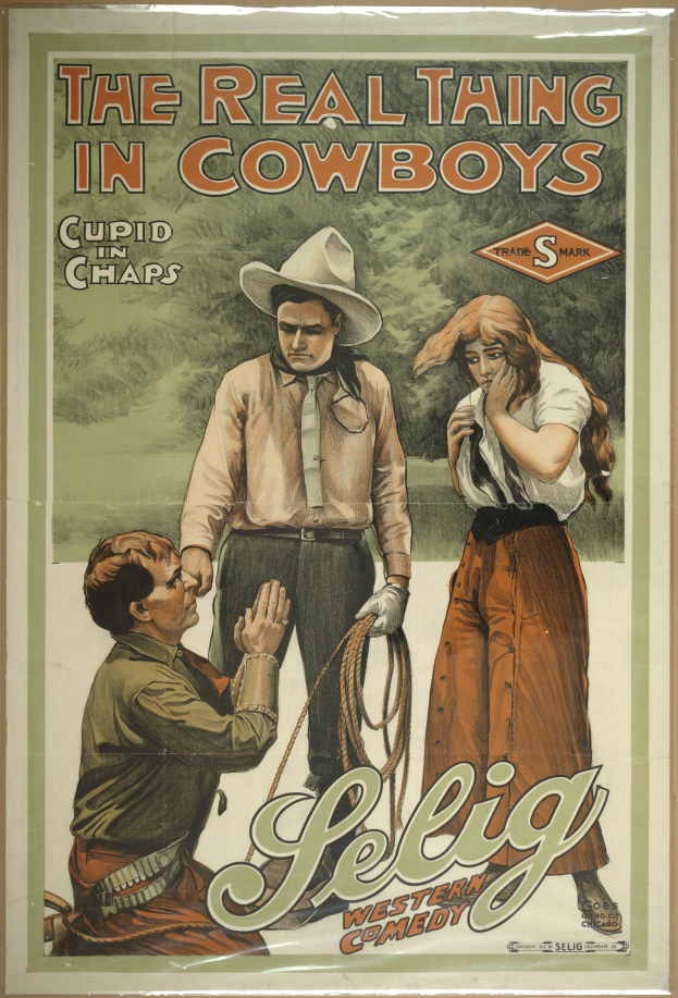 Plakat an einer Wand, das drei Personen zeigt - zwei Männer mit Cowboyhüten und eine Frau in einem langen Kleid - mit der Aufschrift "The Real Thing in Cowboys" in fetter schwarzer Schrift auf einem hellgelben Hintergrund.
