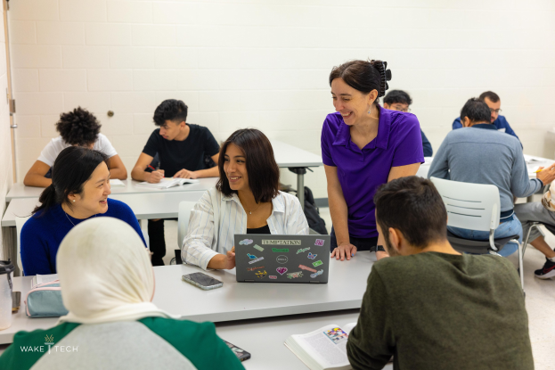 Mitarbeiter sitzen um einen Tisch mit Laptops und Büchern, diskutieren in einem Klassenraum mit einer Tür im Hintergrund.
