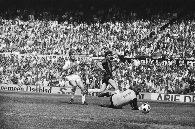 Schwarzes Foto von Männern, die auf einem Feld Füßball spielen, mit Zuschauern im Hintergrund und einem Banner mit der Aufschrift "Bundesliga 1978-79 Ajax 1-1 Hannover 96".