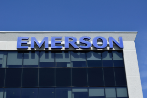 Das Emerson-Logo auf der Seite eines Gebäudes mit dem Text "Emerson investiert $1,5 Milliarden in den USA" vor einem klaren blauen Himmel.