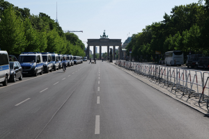 Lange Reihe von Polizeiwagen auf der Seite einer Straße vor dem Brandenburger Tor geparkt, mit Radfahrern, Fußgängern, Barrieren und Bäumen entlang der Straße und dem Torbogen und den Statuen im Hintergrund.