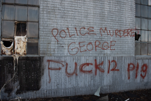 Graffiti an einer Hauswand mit der Aufschrift "Polizei Mord George Fuck 12 P19" mit Fenstern und verstreuten Gegenständen davor.