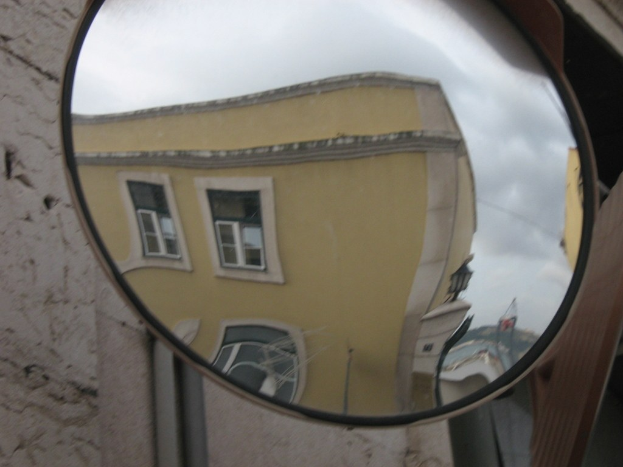 Reflexion von Gebäuden, Licht und Himmel auf einem Straßenverkehrsspiegel mit einer Wand im Hintergrund.