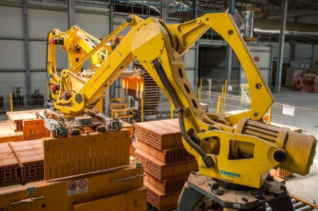 Großes industrielles Lagerhaus mit gestapelten Kisten, Überdachkränen, Zaun, Versorgungsmasten und einer fernen Wand in einer automatisierten Fertigungsanlage.