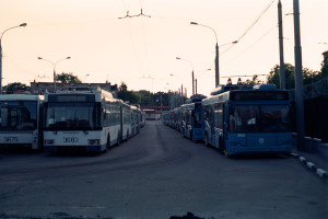 Eine Reihe von Bussen, die entlang einer Straße mit Straßeninfrastruktur und Gebäuden unter einem klaren Himmel geparkt sind.