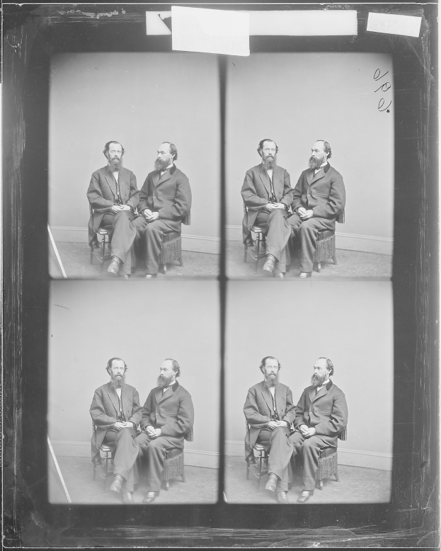 Schwarzes und weißes Foto einer Gruppe von Männern in Anzügen, die in Stühlen sitzen, die in einem Halbkreis angeordnet sind, wobei einige direkt in die Kamera schauen.