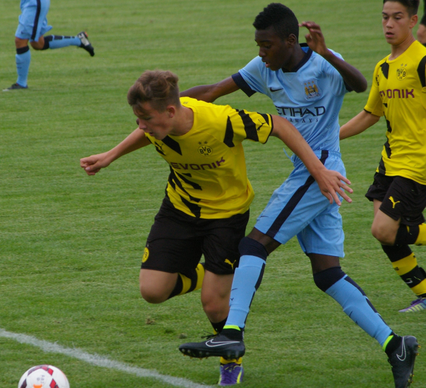 Junge Männer in Sportuniformen spielen Fußball auf einem Rasenfeld während eines Spiels.