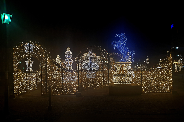 Ein Park bei Nacht mit Weihnachtslichtern in einem dekorativen Muster angeordnet, beleuchtet von einer Straßenlaterne auf der linken Seite.
