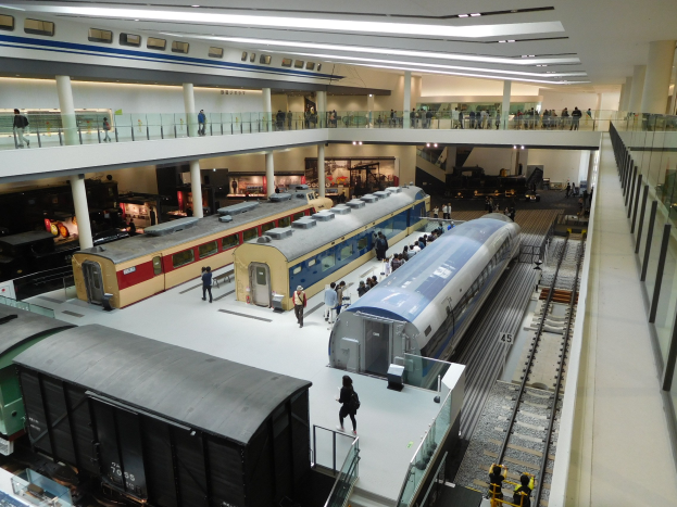 Ein großer Museumsraum mit verschiedenen Bahnen in unterschiedlichen Größen und Farben, mit Menschen, die sie vom Boden, Geländern und Säulen unter Deckenbeleuchtung betrachten.