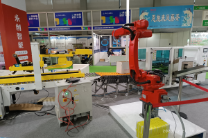 Eine Gruppe von Robotern sitzt an einem Tisch in einer Fabrikumgebung umgeben von Maschinen, Kabeln, Texttafeln und Lichtern, mit Menschen im Hintergrund.