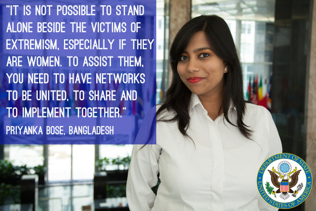 Eine Frau in einem weißen Hemd steht vor einem Gebäude mit einem Zitat über Einheit gegen Extremismus, ein Logo in der rechten unteren Ecke.