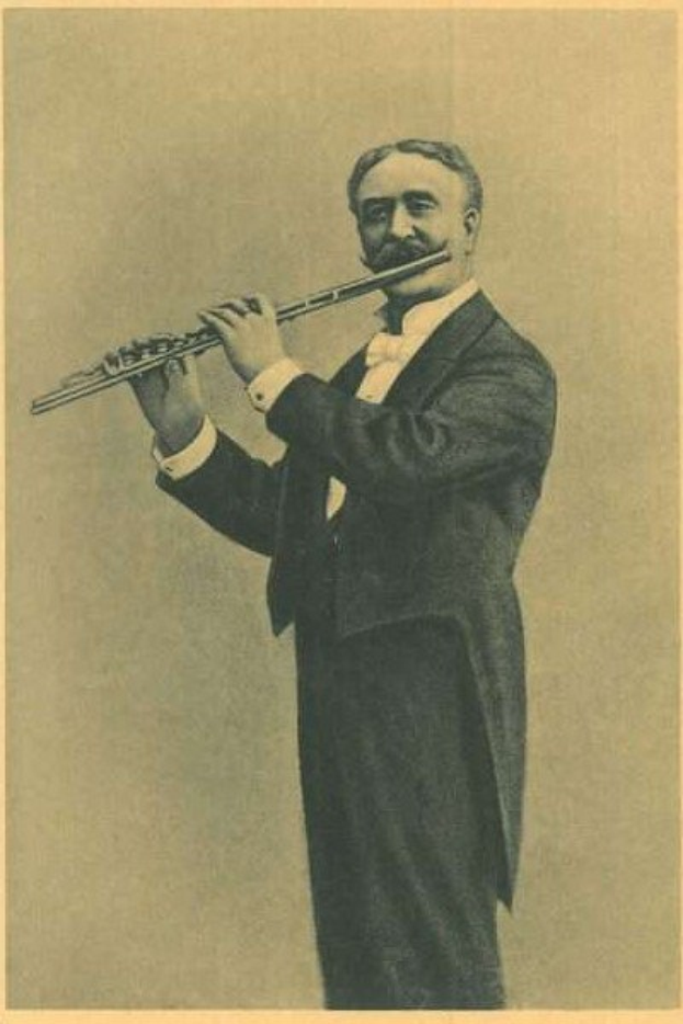 Altes Schwarz-Weiß-Foto eines Mannes in einem Smoking, der auf der Bühne eine Flöte spielt und die Augen geschlossen hat.