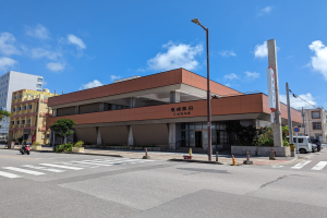 Großes Gebäude mit zahlreichen Fenstern, als die Universität von Hong Kong identifiziert, umgeben von Straßeninfrastruktur, Fahrzeugen und Grünflächen unter einem bewölkten Himmel.