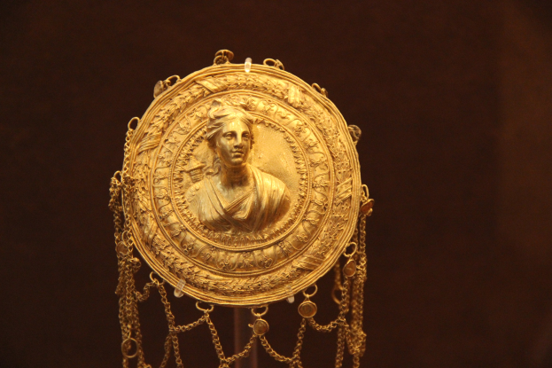 Goldene Medaille mit einer Frauengestalt auf dunklem Hintergrund, mit aufwändigen Details verziert.