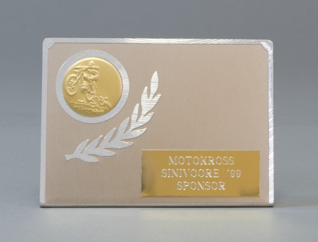 Eine goldene und silberne Visitenkarte mit Lorbeerkranz und Text, mittig auf einem einfarbigen Hintergrund.