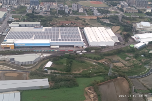 Eine Luftaufnahme eines großen Industriegebiets mit Gebäuden, Bäumen, Gras, Straßen, Fahrzeugen, Polen, Türmen und anderen Gegenständen, mit einem Wasserzeichen in der rechten unteren Ecke, das darauf hinweist, dass es die erste Solarstromanlage in Singapur ist.