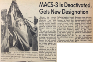 Zeitungstitel 'Macs-3 ist deaktiviert, erhält neue Bezeichnung' mit einer Gruppe von uniformierten Menschen, die ein Tuch halten, lächeln und feierlich wirken, vor einem hellblauen Himmel mit weißen Wolken, mit fetter schwarzer Schrift.